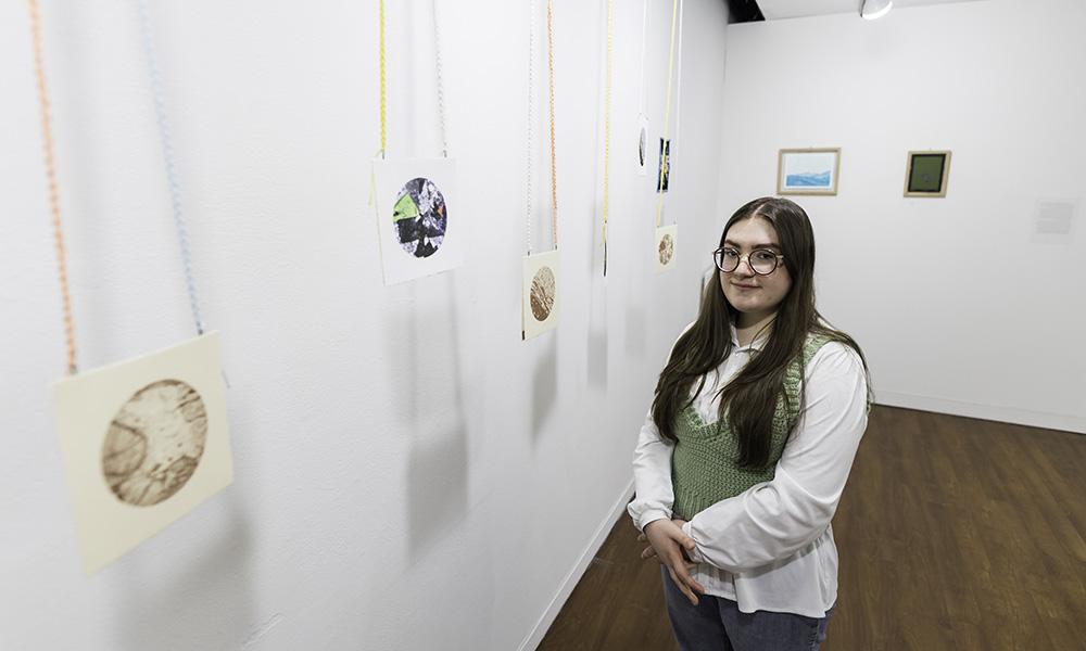 Student stands beside small circular art prints hanging from strings.