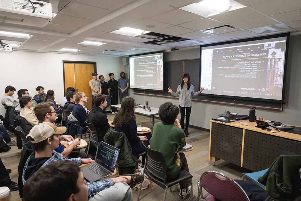 Female PhD student stands before classmates, giving presentation of her group's lens design.