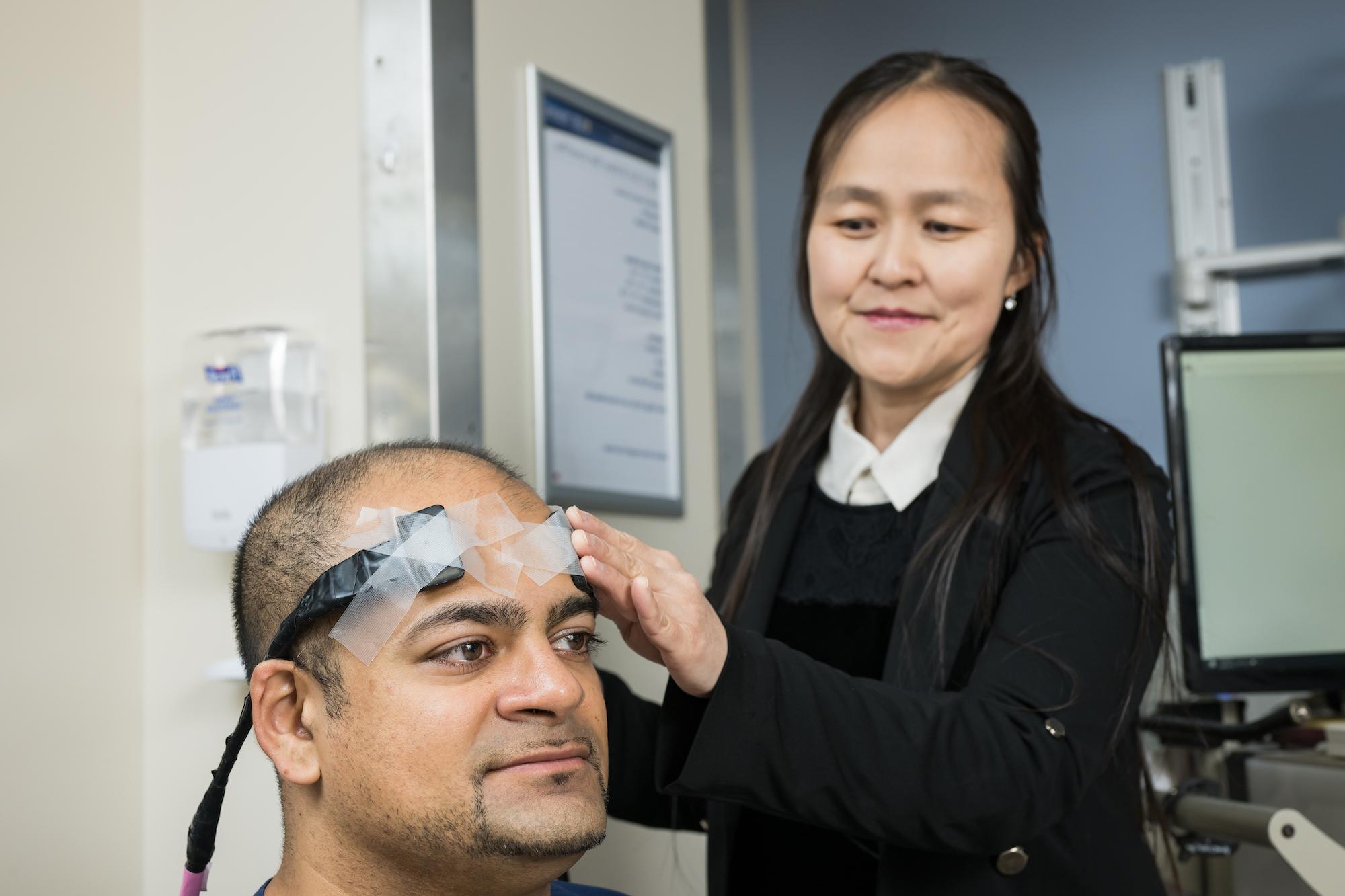 Male researcher models neuro-monitoring device as female researcher affixes device to his head