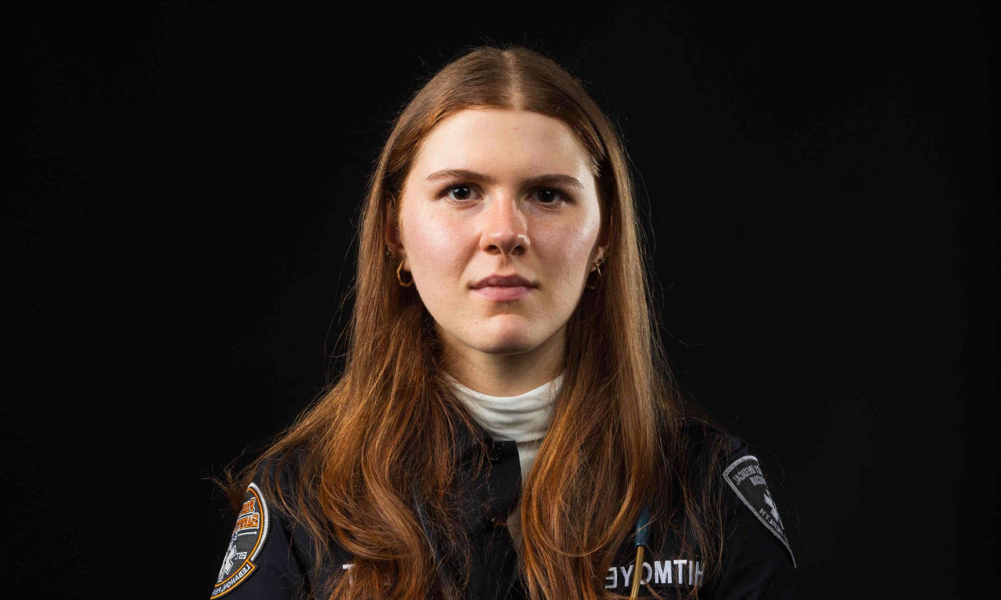Close-up horizontal of Rachel Whitmoeyer against a black background in an EMT uniform staring at the camera.